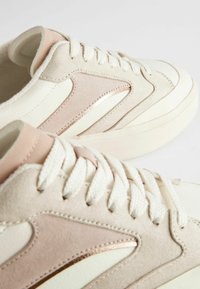 Sneaker beige e rosa con tomaia in pelle e camoscio, caratterizzate da dettagli testurizzati e una suola in gomma bianca. I lacci sono in cotone.