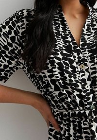 Vestido de estampado en blanco y negro con escote en V, mangas cortas, cierre de botones y cinturilla para una forma ajustada.