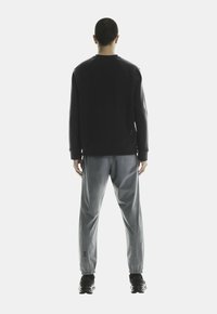 Zwarte crewneck sweatshirt met geribbelde manchetten, gecombineerd met lichtgrijze, taps toelopende trainingsbroek met elastische manchetten en logoprint. Zwarte sneakers.