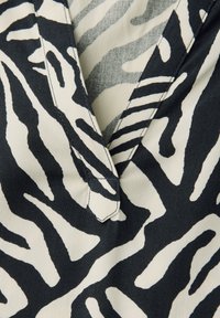 Tessuto in stampa zebra bianco e nero con una consistenza morbida, caratterizzato da una scollatura a V e un dettaglio di cucitura sul collo.