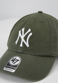 Olivově zelená baseballová kšiltovka s bílou vyšitou logem NY na přední straně. Obsahuje nastavitelný popruh a štítek '47 Clean Up' na okraji.