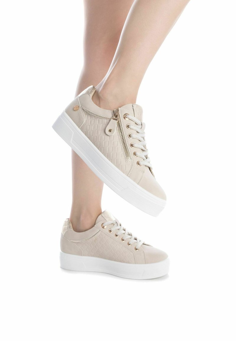 Sneaker beige con texture trapuntata, hardware in tono dorato e suola spessa bianca; presenta lacci e una cerniera laterale per una facile calzata.