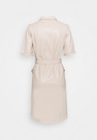 Beige konstläderklänning, knälång med korta ärmar, figurnära midja och sidofickor. Slät textur med en polerad yta.