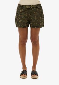 Pantalones cortos cargo de camuflaje verde con cintura ajustable con cordón, bolsillos planos en los laterales y un corte holgado, combinados con sandalias planas negras.