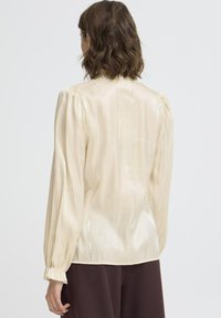 Langærmet bluse i blød cremesatin, der har en subtil glans, samlede pufærmer og en buet kant. Teksturfinish med minimal detaljer.
