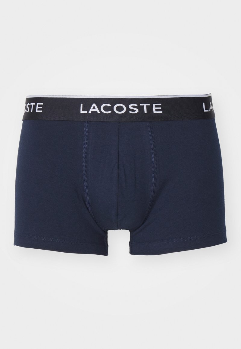 Shorts boxers pour hommes en bleu marine, fabriqués en tissu doux, dotés d'une taille noire avec la marque "LACOSTE" en blanc et des détails de couture contrastants.