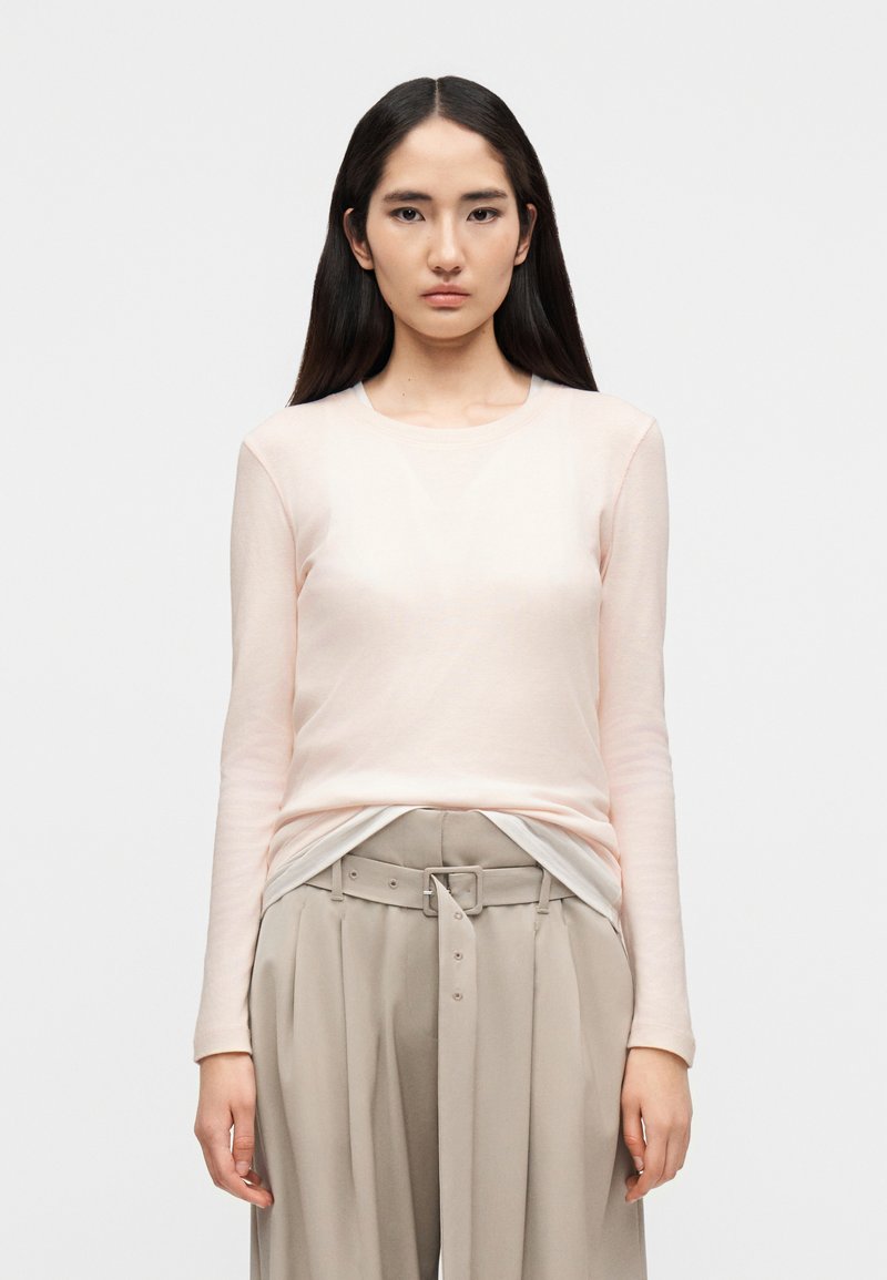 Ανοιχτό ροζ πουκάμισο με μακριά μα νίκια, στρογγυλή λαιμόκοψη, φτιαγμένο από απαλό ύφασμα. Συνδυάζεται με μπεζ παντελόνι ψηλόμεσο με ζώνη και πιέτες.