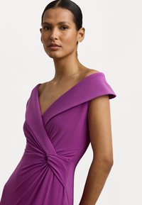 Vestido roxo com um decote em V profundo e alças largas. Apresenta um detalhe de tecido torcido na cintura e uma textura suave e elástica.