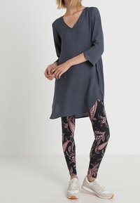 Ciemnoszara, luźna tunika z dekoltem w serek; w duecie z czarnymi legginsami w różowe wzory paisley; całość uzupełniona jasnymi trampkami.