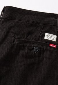 Poche arrière d'un pantalon en velours côtelé noir Levi's avec fermeture à bouton, écusson de la marque blanc et étiquette rouge du logo Levi's.