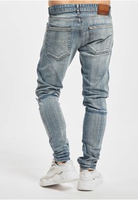 Lyseblå denimjeans med smal passform, med to baklommer og en skinnetikett på midjebåndet. Kombinert med hvite joggesko.