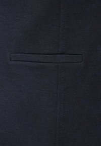 Mörk marinblå texturerad tyg med en horisontell ficka och synlig vertikal söm på höger sida.