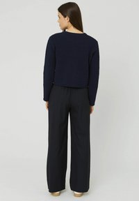 Pull en maille cropped bleu marine avec un tissu texturé, associé à un pantalon large à rayures noires. L'ensemble comprend des manches longues et un col rond.