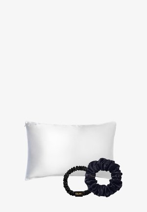 Witte zijden kussen met een gladde textuur, vergezeld van twee satijnen haarscrunchies: één zwart en één donkerblauw.
