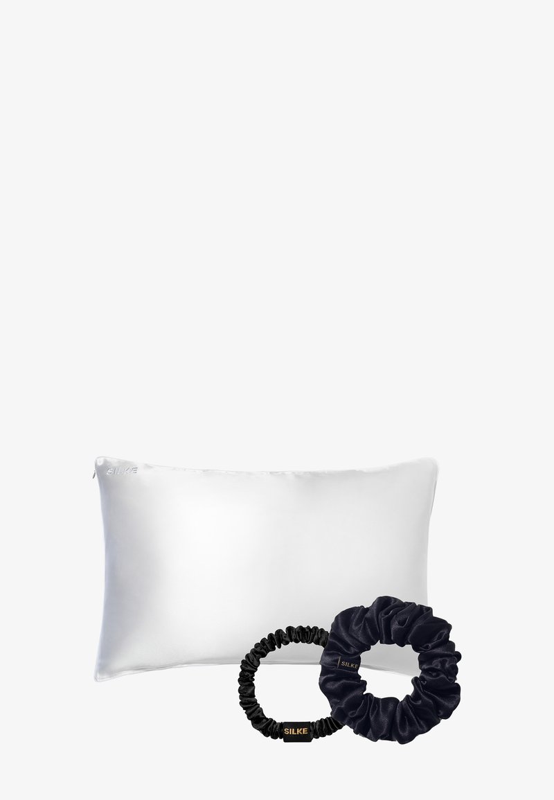 Almohada de seda blanca con una textura suave, acompañada de dos coleteros de satén: uno negro y uno azul marino oscuro.