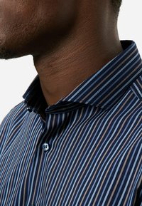 Marineblaues und hellblau gestreiftes Hemd mit einem Button-down-Kragen und einem Einzelknopf-Detail, aus einem glatten, strukturierten Stoff gefertigt.