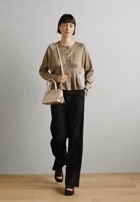 Haut beige à manches longues texturé avec des boutons, associé à un pantalon noir à taille haute et à jambe large. Accessoirisé avec un petit sac à main beige.