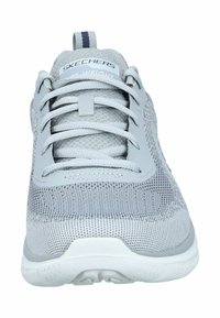 Chaussure de sport grise avec une tige en maille texturée, un bout rond, des accents synthétiques et une semelle blanche. Dispose de lacets et d'une languette au talon.