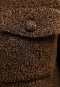 Brązowa dzianina z teksturowaną powierzchnią, z okrągłym guzikiem i kieszenią z klapką.