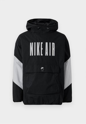 Casaco impermeável preto com capuz, apresentando "NIKE AIR" em grandes letras brancas. Detalhes cinzentos nos ombros e um bolso frontal tipo pouch. Design elegante.