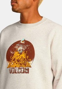 Sudadera gris con un diseño gráfico colorido que presenta un pájaro y patrones en espiral. Texto "VOLCOM" en negrita en la parte inferior.