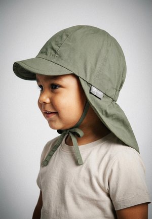 Young child wearing a light beige shirt and an olive green sun hat with neck flap and chin ties, smiling and looking to the side.