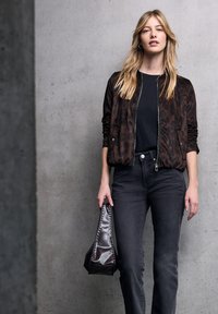 Bomber jacket con stampa leopardata marrone, t-shirt nera, jeans grigi attillati e una borsa di pelle scura con bordo cucito tenuta in una mano.