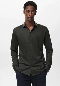 Camisa de manga larga verde oscura en una tela suave con cuello de punta, frente abotonado y diseño ajustado. Acentuada con botones sutiles.