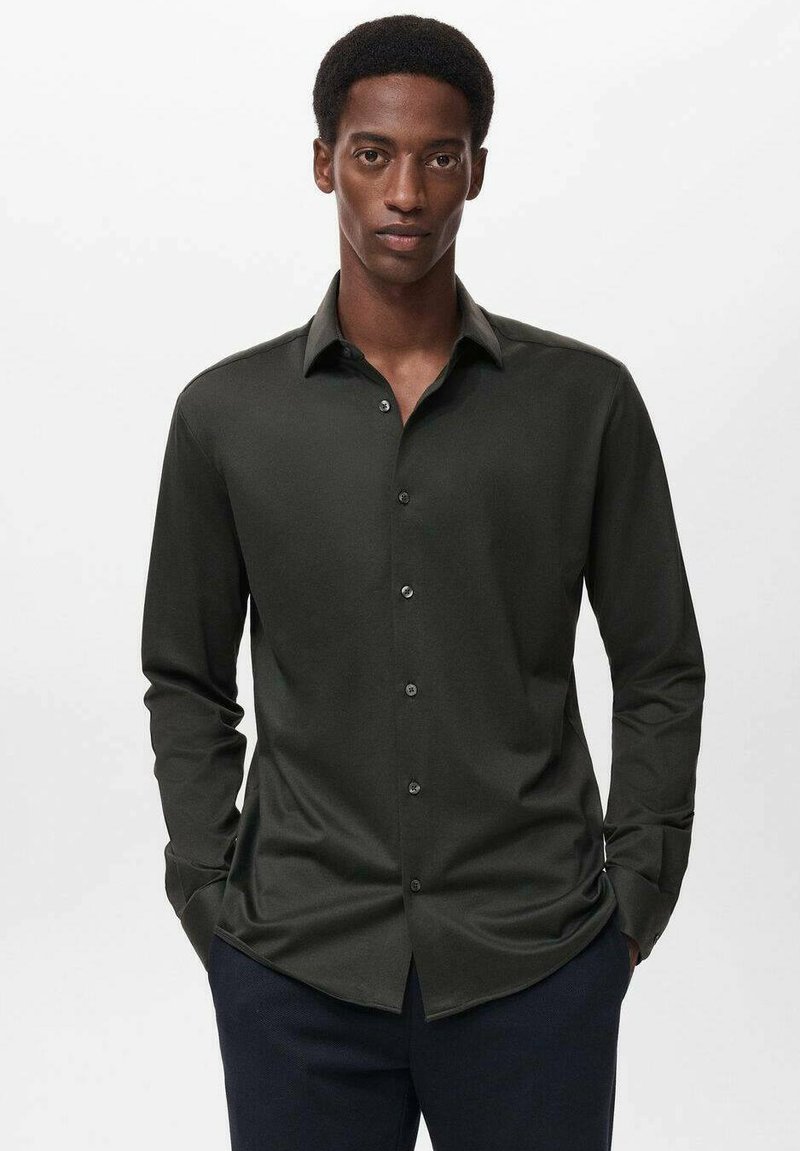 Camisa de manga larga verde oscura en una tela suave con cuello de punta, frente abotonado y diseño ajustado. Acentuada con botones sutiles.
