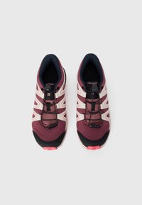 Chaussures de course avec une tige en maille bordeaux, une semelle extérieure en caoutchouc noir, des accents blancs et des lacets élastiques ; elles disposent d'un col et d'une languette rembourrés.