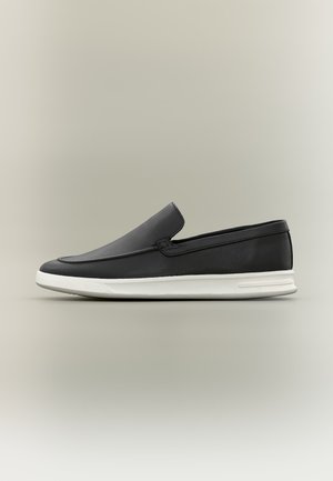 Mocassin en cuir noir à enfiler avec dessus texturé et semelle en caoutchouc blanche, présenté de profil sur un fond neutre.