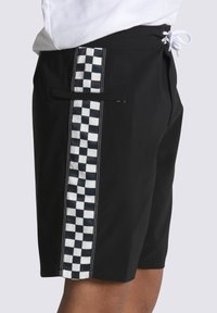 Pantaloni da nuoto neri con motivo a scacchi bianco e grigio sui lati. Presentano una vita con cordoncino e una tasca sul retro.
