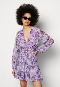 Top crop floral roxo com decote em V profundo e mangas bufantes longas, combinado com uma saia mini franzida correspondente com unha bainha em camadas.
