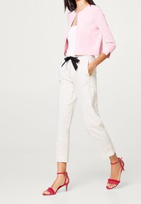 Cárdigan corto rosa claro, camiseta sin mangas blanca, pantalones crema a rayas de talle alto con lazo negro y sandalias de tacón rosas.