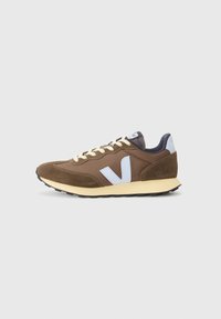 Brown sneaker featuring a mesh upper, suede accents, cream laces, a light blue logo, and a black rubber sole.