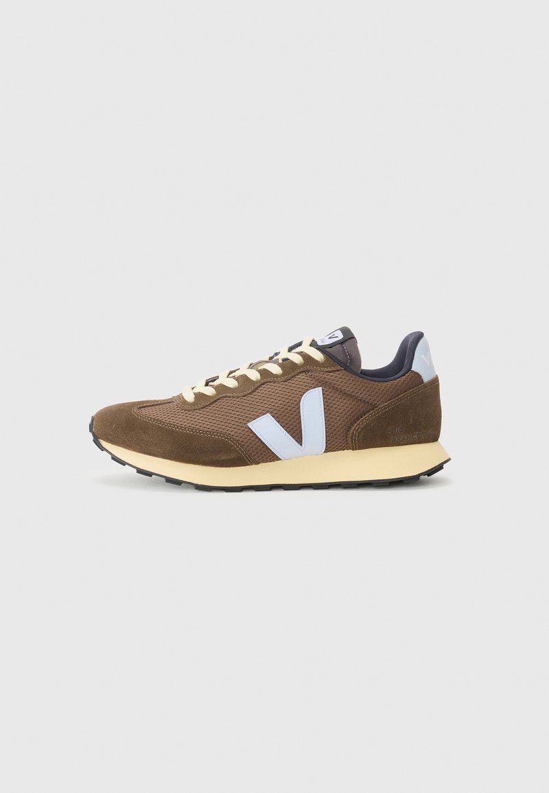 Brown sneaker featuring a mesh upper, suede accents, cream laces, a light blue logo, and a black rubber sole.