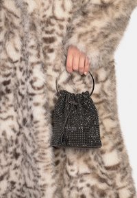 Zwarte tassenemmer met trekkoord en zilverkleurige ronde handgreep, vastgehouden naast een lichtbruine, gevlekte nepbontjas.