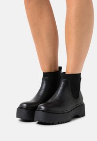 Bottines Chelsea noires avec une semelle plateforme épaisse, en matériau semblable au cuir lisse, avec des panneaux latéraux élastiques et une finition mate.