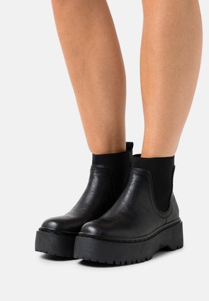 Bottines Chelsea noires avec une semelle plateforme épaisse, en matériau semblable au cuir lisse, avec des panneaux latéraux élastiques et une finition mate.