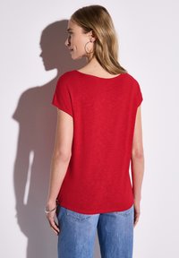 Rotes kurzärmeliges Oberteil mit weiter Halslinie, aus leichtem Stoff. Kombiniert mit hellblauen Jeans, die einen lockeren Sitz zeigen.