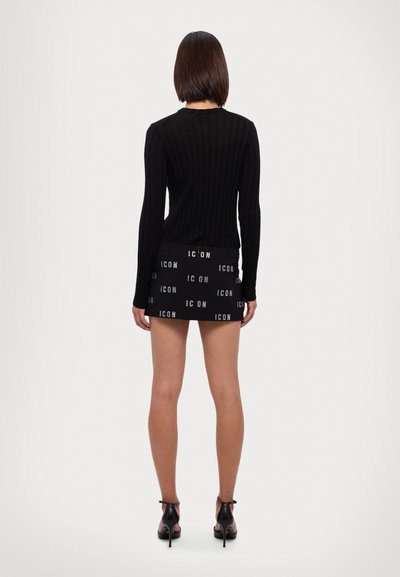 Zwarte geribbelde lange mouw top gecombineerd met een zwarte mini rok met een herhaald "ICON" logo patroon, afgemaakt met zwarte hoge hakken.