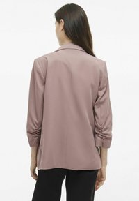 Světle růžový, texturovaný blazer s volným střihem, tříčtvrtečními rukávy a klopovým límcem. Hladká tkanina a minimalistický design.