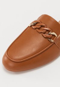 Nahan nahka loafer pyöristettyllä varvalla, jossa on paksu ketjdetalli ruskealla ja kullalla korostettuna. Sileä rakenne, minimalistinen muotoilu.