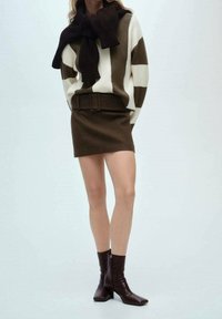 Pull en maille à rayures marron et crème avec un nœud au col, assorti à une mini-jupe marron et des bottines à talons blocs marron.