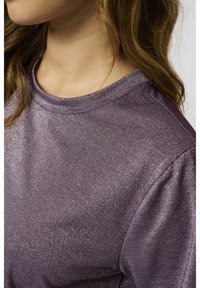 Lila metallisk kortärmad topp med rund halsringning. Tyget har en glittrande textur och visar fina, horisontella ränder.