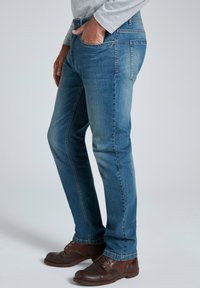 Jeans de denim azul claro de corte slim, con cinco bolsillos, trabillas para el cinturón y una textura desgastada. Llevado con zapatos marrones de cordones.
