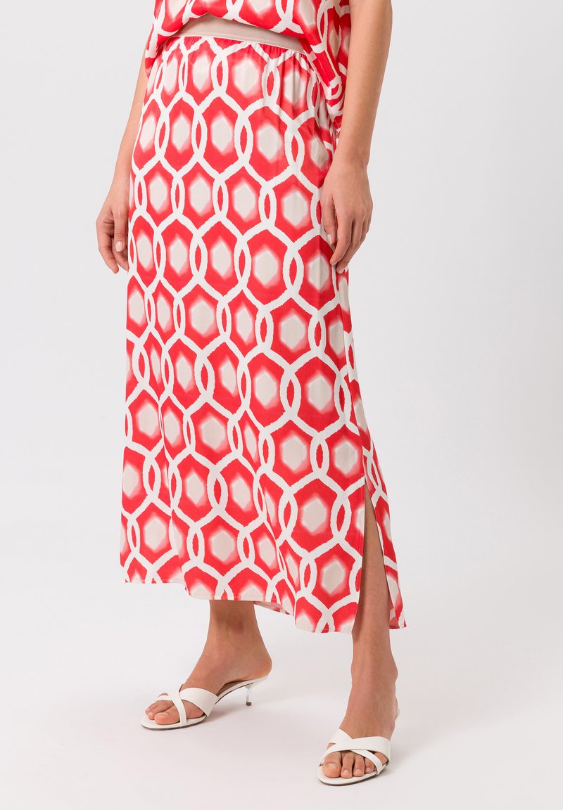 Jupe maxi rouge avec un motif géométrique d'ovales blancs entrelacés. Présente une fente sur le côté et une taille élastique, fabriquée en tissu léger.