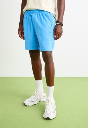 Light blue athletic shorts with an elastic waistband and a small logo. Worn with white ankle socks and chunky white sneakers.