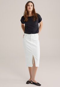 Čierny top s krátkym rukávom skombinovaný s bielou denimovou sukňou so štrbinou vpredu. Model má na sebe čierne sieťované slip-on topánky. Minimalistický dizajn.