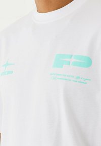 Camiseta blanca de algodón de manga corta, con texto gráfico y logo en azul claro en la parte delantera. Textura suave, diseño de cuello redondo.